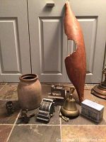 Full lot showing large wooden paddle, pottery jar, toy sewing machine, mechanical calculator, brass bell, metal tin, and small decorative pieces on tiled floor.