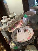 Multiple porcelain tea cups, saucers, plates, serving dishes and relief cachepot grouped on glass shelf