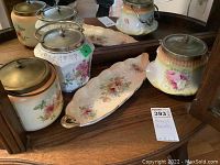 Set of three biscuit barrels and one matching floral ceramic tray on wooden surface with mirror background.