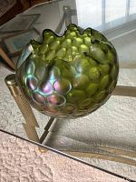 Photo of green hobnail textured carnival glass bowl with ruffled edge on a glass table.