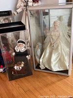 Photo showing both collector dolls in their cases, with the Princess Grace doll in a glass case and Christmas girl doll in a plastic case