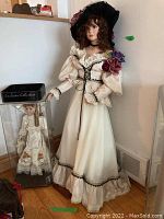 Full view of both dolls together, one large standing on wooden base and one in hexagonal plastic display case