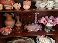 Assorted frilled glass pieces on wooden shelf: pitchers, bud vases, ruffled bowls