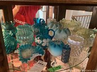 Photo showing a variety of frilled edge glass bowls and vases in blue, white, and green colors on a glass shelf.