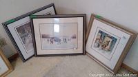 Three framed prints leaning against wall on carpet