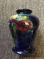 Side view of vase showing detailed raised floral design with multi-colored glazing on deep blue background.