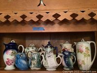 Shelf display of nine assorted ceramic pots and pitchers, showing full lot.
