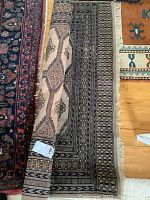 Photo showing Persian rug partially rolled with visible geometric designs and damaged fringe.