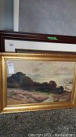 Framed landscape painting with coastal scene, clearly showing the gold frame and part of the image.