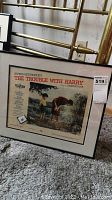 Framed color poster of Alfred Hitchcock's The Trouble With Harry in black frame with white matting, showing the entire poster and frame on carpet.
