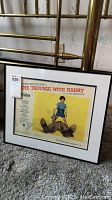 Framed poster of The Trouble With Harry leaning against brass bed, showing the full image and frame.