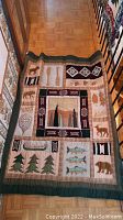 Full view of handmade quilt laid out on hardwood floor hallway showing entire design with stitched patches of animals, trees, fish and paddles.