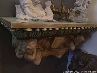 Front and side views of ornate wall-mounted shelf showing cherub figures and leafy trim with chipping visible.