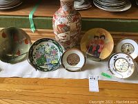 Photo showing oriental vase surrounded by decorative plates arranged on stands and stacked, illustrating overall lot composition