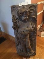 Front view of the rectangular wall decor panel showing the cherub figure in bas relief with intricate leaf and swirl designs.