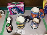 Photo showing Wonder Woman metal lunchbox, Superman mug with 3D figure on handle, Batman mug with logo,and two Betty Boop ceramic items including shoe figure and a mug.