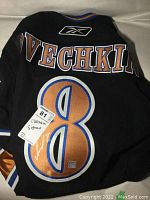 Back of black Capitals jersey showing OVECHKIN name and number 8 with signature and lot sticker.