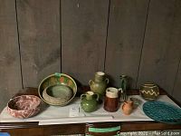 Wide view showing all pottery items, including bowls, pitchers, and vases arranged on a flat surface against a wood backdrop