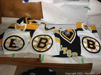 Four jerseys laid flat on couch: three white Bruins and one black Penguins.