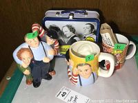 Photo showing the Three Stooges figurine, two mugs (one Three Stooges themed and one Dagwood themed), and the Three Stooges metal lunchbox in the background.