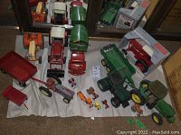 Overview of lot on fabric backing showing 12 toy tractors, wagons, trailers; one boxed item