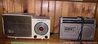 Two vintage radios on wooden shelf: General Electric Musaphonic radio on the left, silver portable cassette recorder radio on the right.