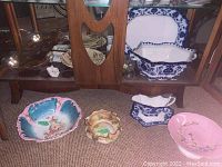 Photo showing assorted vintage serving ware including Nippon and F & Sons Oxford Burslem pieces arranged on floor in front of cabinet