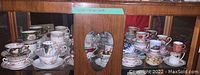 Displays all the tea cup and saucer sets arranged in wooden shelving with glass front