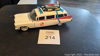 Side angle showing full length of white Cadillac ambulance with Ghostbusters logo on door and roof equipment.