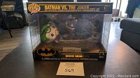 Front view of unopened Funko Pop! Heroes Movie Moments Batman vs. The Joker set showing the figures inside a clear plastic box with black display base and Batman logo.