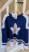 Front view of blue Toronto Maple Leafs hockey jersey with white maple leaf logo with text and sleeve logos.