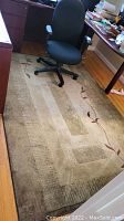 Full view of the machine made area rug under office chair and desk showing geometric pattern and leaf border design.