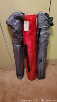 Three camping chairs rolled inside their original carrying bags, two gray and one red.