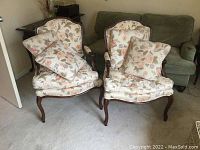 Two matching floral upholstered armchairs each with a square throw pillow