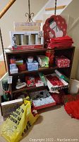 Wood shelving unit with multiple Christmas-themed tins and boxes, vintage linens including red towels, LED pillar candles in original box, and snowman serving plate stacked on top.