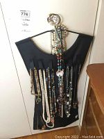 Photo of hanging black fabric jewelry organizer with multiple costume necklaces including faux pearls and beaded styles.