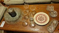 Photo of entire lot on wooden table showing crystal bowls, etched glasses, silverplate coasters, hand painted plate, and clear glass ashtrays