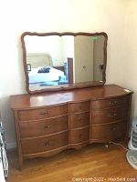Front view of the Malcolm nine-drawer dresser with the matching scalloped framed mirror resting on top. The surface shows scratches and some wear.