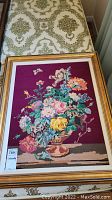 Full view of the framed floral embroidery artwork on a patterned fabric surface.