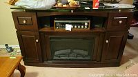 Full view of dark wood cabinet with built-in electric fireplace insert, stereo receiver on top shelf, and drawers and cabinets.