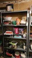 Full view of shelving unit with various kitchenware including mixing bowls, chopper, roaster, stock pots, and boxes of kitchen products.