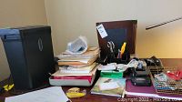Photo showing a black paper shredder, office supplies in trays, and paper stacks on a desk.