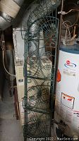 Photo showing tall green metal garden trellis with scroll and fan decorative elements leaning against a wall near dryer and water heater.