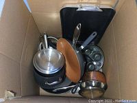 Top view of pots and pans including copper saucepan, non-stick fry pans, egg poacher, and baking tray in a box