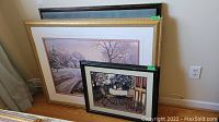 Three framed wall art prints leaned against a wall, showing two fronts and one back print, various sizes.