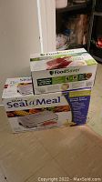Rival Seal-a-Meal box and FoodSaver rolls box grouped together on floor
