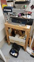 Full view of Ryobi 16-inch scroll saw mounted on wooden bench with box underneath containing various items and tools on top.