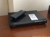 Sony black DVD player with remote placed on top, showing front panel with branding and controls.