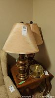 Photo showing two matching table lamps with beige fabric shades and brass bases on a wooden stand, alongside a small brass and glass ceiling light fixture.