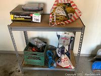 Shelf with bags of road salt, ropes, green plastic crate with various hand tools and cords.